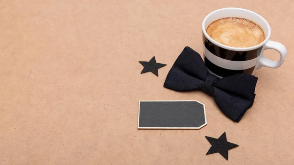 Happy Father's Day Background. Cup of coffee and black bow tie on brown background flat lay. Fathers day still life.