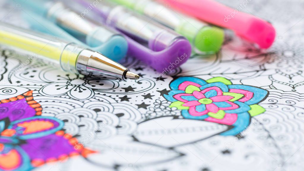 Adult coloring book, new stress relieving trend. Art therapy, mental health, creativity and mindfulness concept. Adult coloring page with pastel colored gel pen close up.