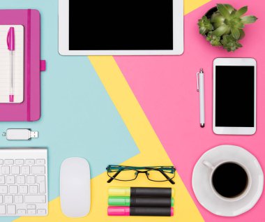 Ofis Masası çalışma alanı düz yatıyordu. Çalışma alanı ile tablet ve smartphone, kahve fincanı, klavye, Not defteri ve çok renkli pastel zemin üzerine etli bitki boş sahte fotoğrafı üstten görünüm.