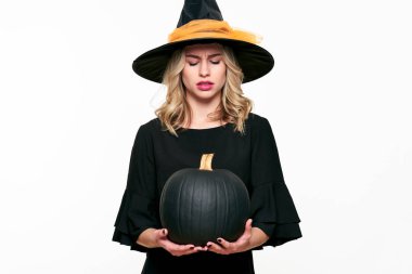 Kızgın Cadılar Bayramı büyük siyah kabak holding, bakınca cadı. Güzel genç kadın cadı şapka ve balkabağı beyaz arka plan üzerinde tutarak kostüm.