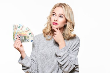 Genç güzel kadın düşünme Euro banknot demet holding, çene, beyaz arka plan üzerinde izole el ile yukarı bakıp kazağı gri.