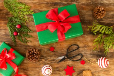 DIY hediye. Rustik ahşap masa üzerinde kırmızı yay ile güzel yeşil Noel hediyeleri. Üstten görünüm Noel İstasyonu kaydırma.