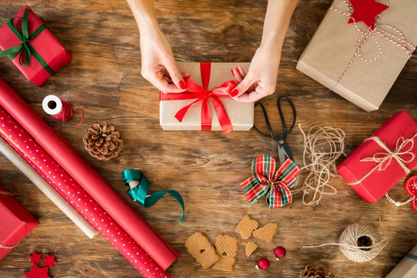 DIY Gift Wrapping. Woman wrapping beautiful christmas gifts on rustic wooden table. Overhead view of christmas wrapping station.