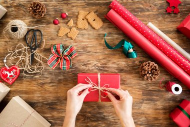 DIY Gift Wrapping. Woman wrapping beautiful red christmas gifts on rustic wooden table. Overhead point of view of christmas wrapping station. clipart