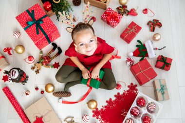 Meraklı kız katta oturan xmas kostüm Ren geyiği boynuzları giyiyor Noel hediyesi, en iyi görünümü açma.