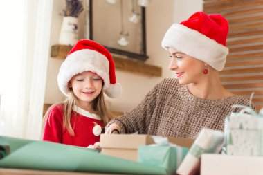 Anne ve kızı Noel hediyeleri birlikte oturma odasında kaydırma eğleniyor santa şapka giymiş. Samimi aile Noel zaman yaşam tarzı geçmişi.