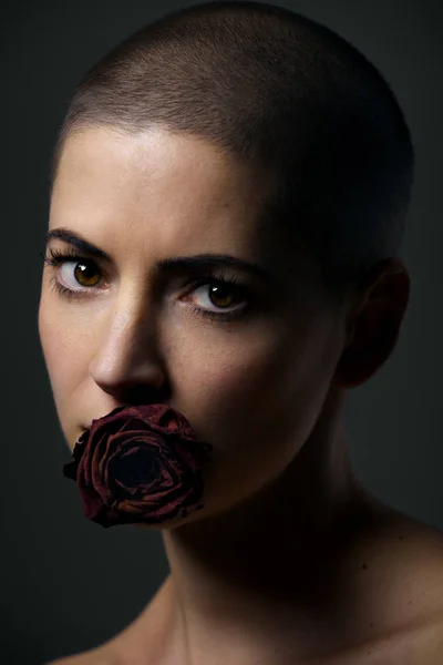 Beautiful female cancer patient with shaved head and rose in her mouth. Cancer taboo, equality and discrimination by society concept.
