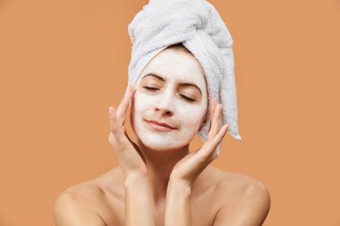 Young woman with closed eyes and peaceful facial expression wearing mouisturizing facial mask on her face. Wellness and Spa concept on beige background.  clipart