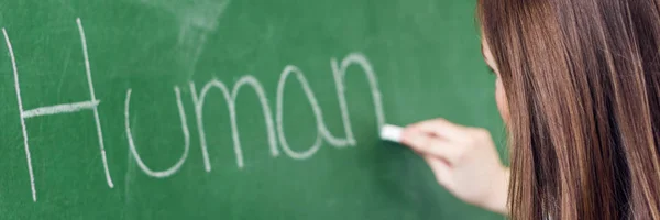 Young female teacher teaching in biology class. Teacher writing Human Body on blackboard using chalk.