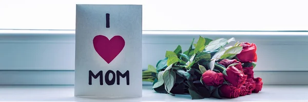 Happy Mother's Day or Birthday Banner. Homemade greeting card and bouquet of red roses on window sill.