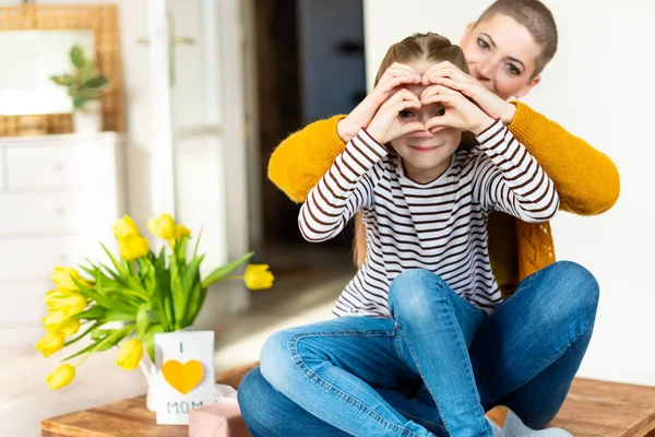 Mother and daughter looking through heart shaped love symbol hand gesture. Family, love, togetherness concept.