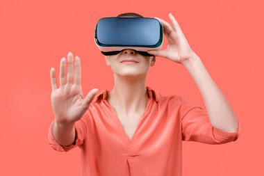 Young woman wearing virtual reality goggles. Woman wearing VR glasses over coral background. VR experience concept.