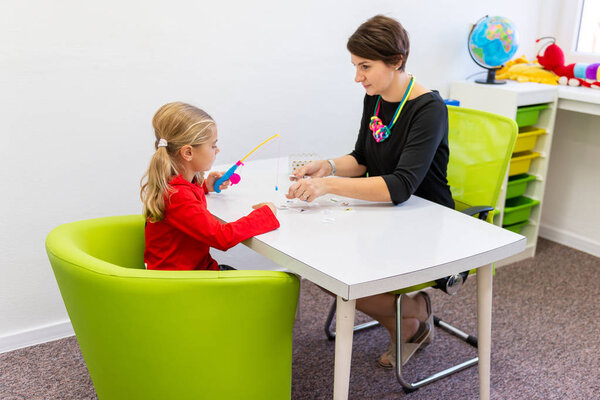 Elementary Age Girl in Child Occupational Therapy Session Doing Playful Exercises With Her Therapist. 