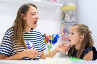 Çocuk konuşma terapisi konsepti. Anaokulu öğrencisi bir kadın konuşma terapistiyle doğru telaffuz pratiği yapıyor.. 
