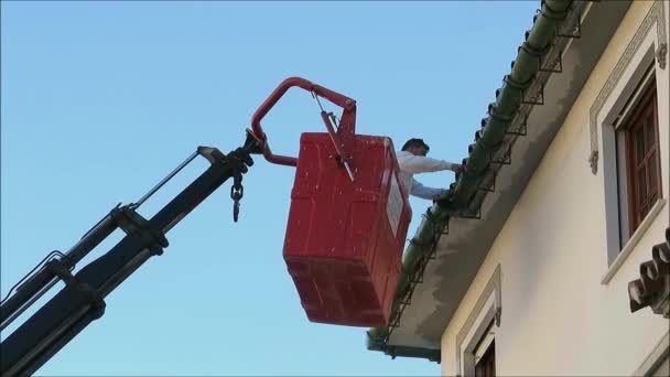 西班牙阿拉拉 2018年11月30日 男子用钢桶清扫悬挂在起重机吊臂上的高大村舍的排水沟 — 图库视频影像