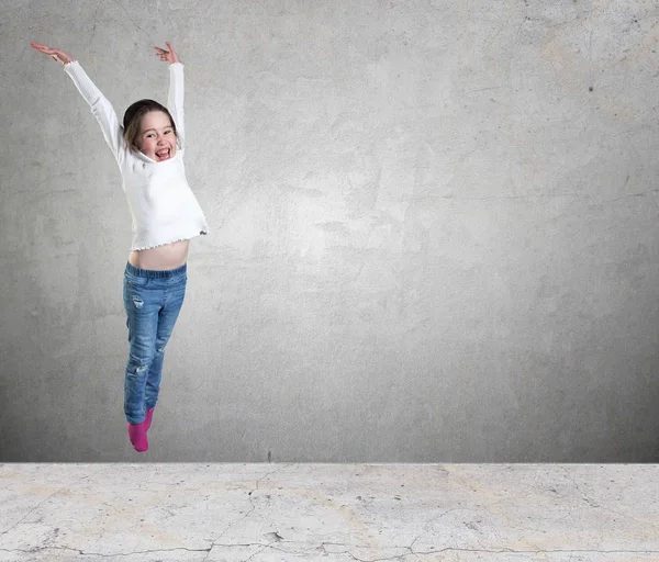 Щаслива маленька дівчинка стрибає в повітрі на фоні бетонної стіни — стокове фото