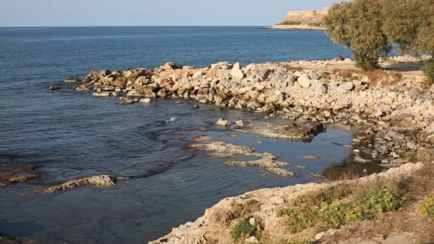 Felsige Küste eines blauen Meeres mit der antiken Festung von Rethymno im Hintergrund unkonzentriert — Stockvideo