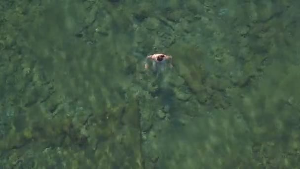 Όμορφη νεαρή γυναίκα σε ένα κολυμπώντας κοστούμι απολαμβάνει κολύμπι στην πεντακάθαρη θάλασσα — Αρχείο Βίντεο