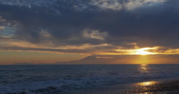 바다와 산 배경에서 황금 태양 반사와 함께 해변에서 아름 다운 석양 — 비디오