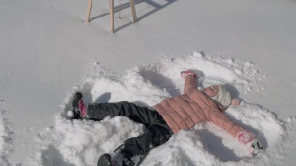 Schönes kleines Mädchen, das einen Schnee-Engel macht — Stockvideo