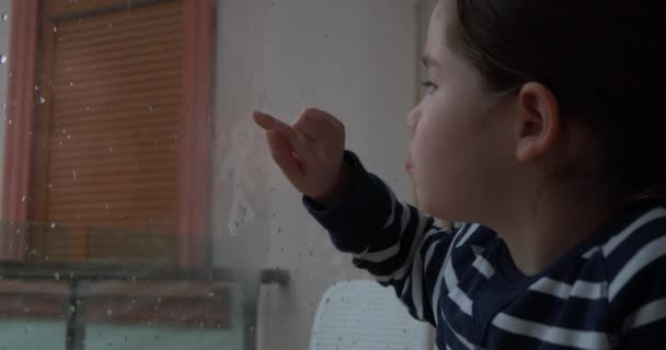 A little girl draws on the window in rainy day — Stock Video