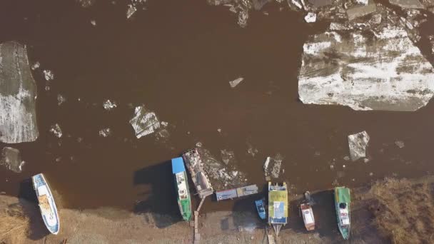 Некоторые лодки на берегу реки, в то время как лед дрейфует весной — стоковое видео