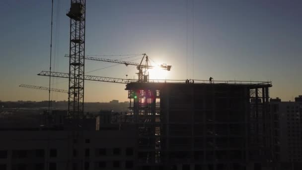 Будівельний майданчик на заході сонця. Силует будівельного крана біля будівлі — стокове відео