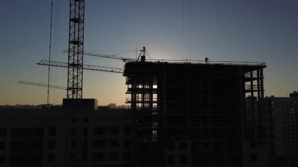 Placu budowy o zachodzie słońca. Sylwetka żurawia budowlanego w pobliżu budynku — Wideo stockowe