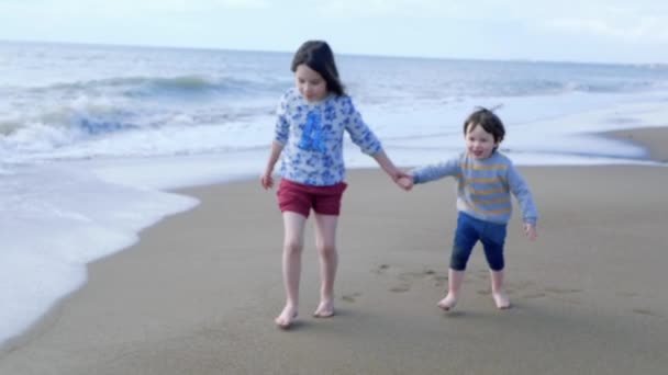 Ευτυχισμένα παιδιά που παίζουν στην παραλία. Η αδελφή και ο μικρός της αδελφός τρέχουν κρατώντας τα χέρια — Αρχείο Βίντεο