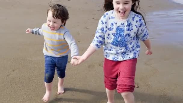 Niños felices jugando en la playa. Hermana y su hermano pequeño corren tomados de la mano — Vídeos de Stock