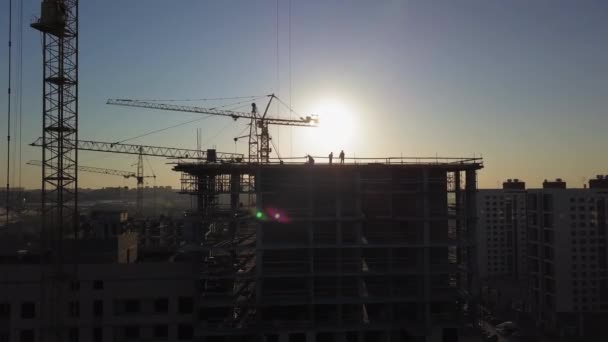 Bouwplaats bij zonsondergang. Silhouet van een bouwkraan in de buurt van het gebouw — Stockvideo