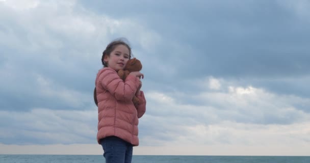 Little girl hugs a teddy bear on the beach — Stock Video