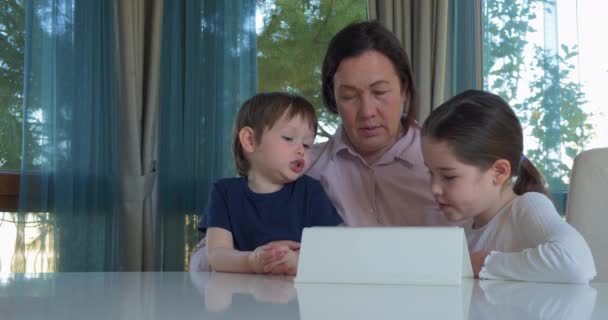 Oma unterhält ihre kleinen Enkel mit einem Tablet-Computerspiel — Stockvideo