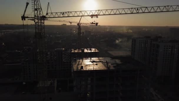 Bouwplaats bij zonsondergang. Silhouet van een bouwkraan in de buurt van het gebouw — Stockvideo