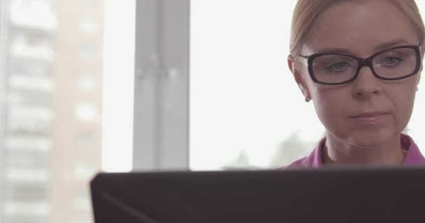 Ritratto di donna sorridente che indossa occhiali da lavoro a casa con un computer portatile — Video Stock