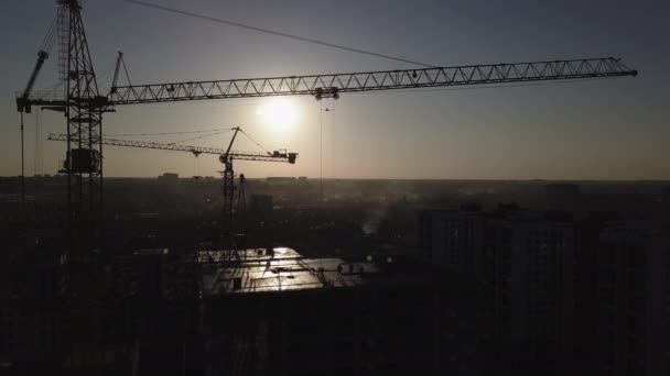 Будівельний майданчик на заході сонця. Силует будівельного крана біля будівлі — стокове відео