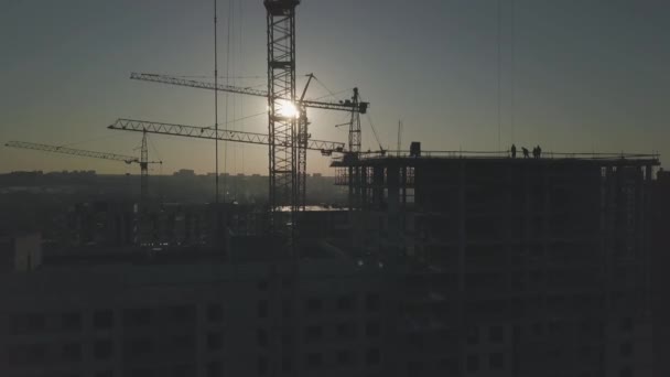 Bygg arbets plats vid solnedgången. Silhuett av en byggkran nära byggnaden — Stockvideo