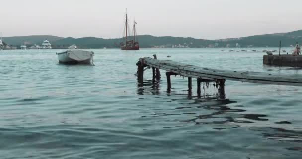 Een boot gebonden aan een houten pier in de zee in de avond — Stockvideo