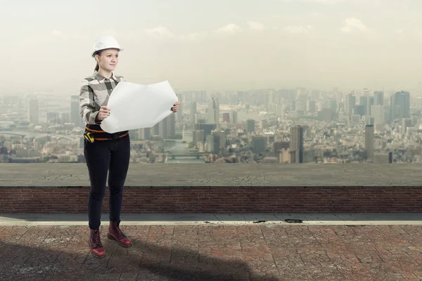 Ingegnere donna che tiene piani di costruzione in piedi sul tetto sopra una città — Foto Stock