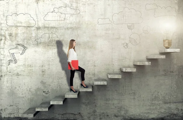 Side view of young businesswoman climbing the stairs with idea lamp on concrete background — Stock Photo, Image