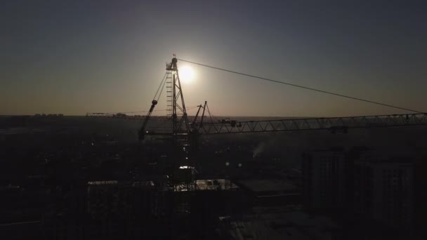 Építőipari site naplementekor. Egy építési daru sziluettje az épület közelében — Stock videók