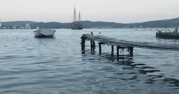 Een boot gebonden aan een houten pier in de zee in de avond — Stockvideo