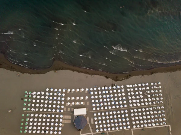 Вид с воздуха на песчаный пляж с шезлонгами и белыми зонтиками на закате — стоковое фото
