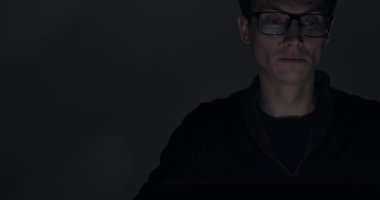 Karanlık odada gece geç saatlerde dizüstü bilgisayar üzerinde çalışan bir adamın portresi