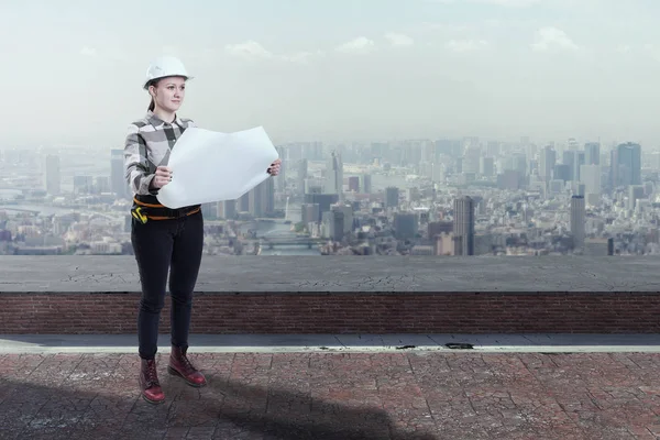 Ingegnere donna che tiene piani di costruzione in piedi sul tetto sopra una città — Foto Stock