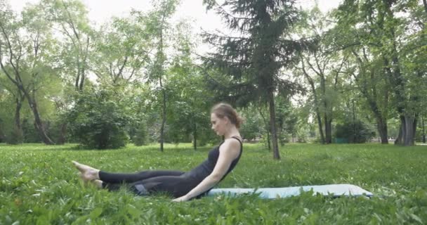 Όμορφη γυναίκα κάνει Πιλάτες στο πράσινο πάρκο — Αρχείο Βίντεο
