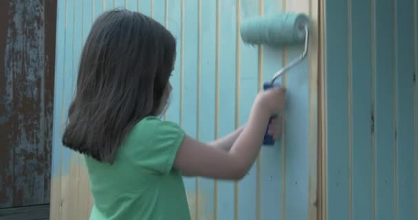 Jong meisje schilderij kleine houten huis met een roller — Stockvideo