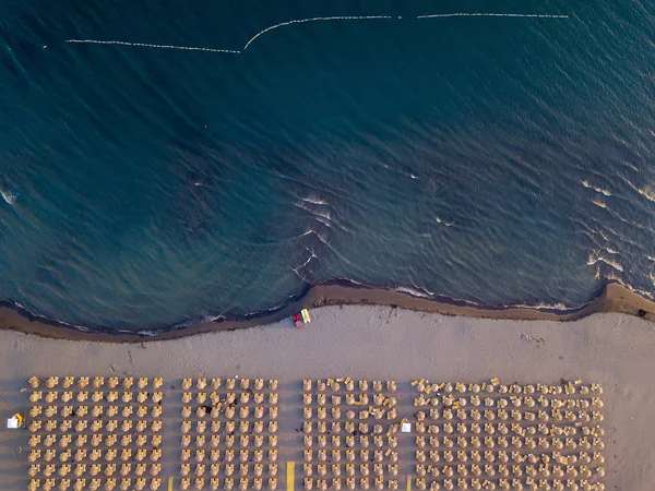 Вид с воздуха на песчаный пляж с желтыми шезлонгами и деревянными зонтиками на закате — стоковое фото