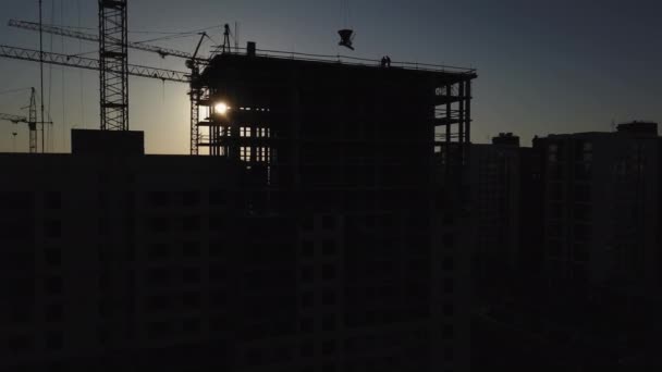 Chantier de construction au coucher du soleil. Silhouette d’une grue de construction près du bâtiment — Video