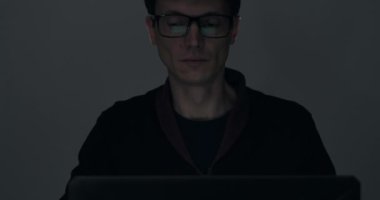 Karanlık odada gece geç saatlerde dizüstü bilgisayar üzerinde çalışan bir adamın portresi